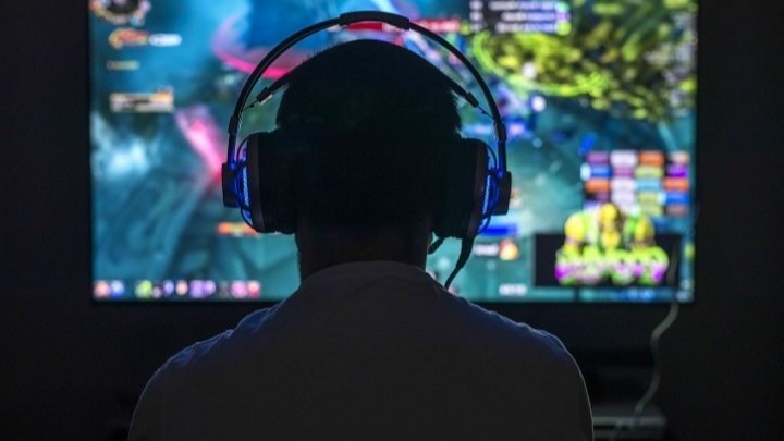 Silhouette d'un joueur portant un casque audio, de dos, face à un grand écran de jeu